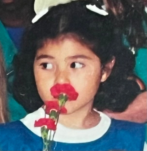 An Introvert mixed Brown six year old girl smells a red Carnation flower to find comfort at this busy social gathering